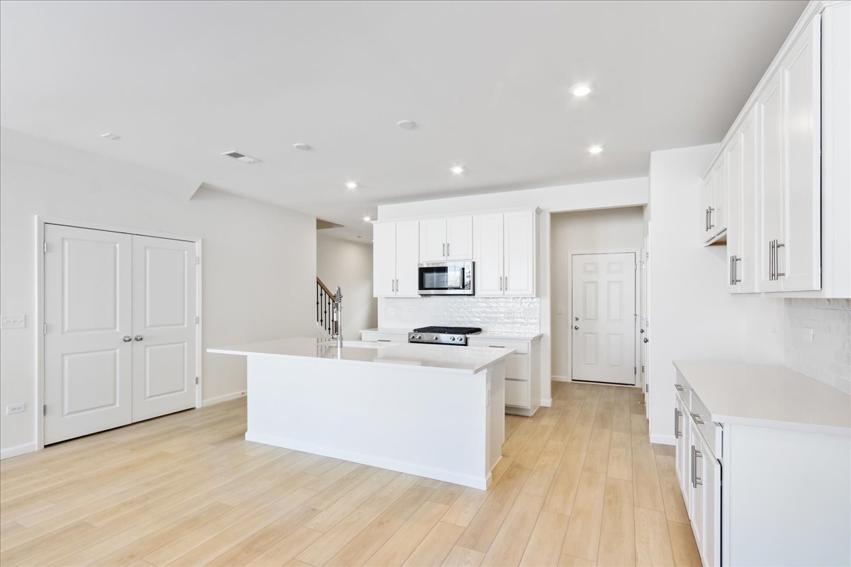 644 Switchgrass Way, Unit 59002 Bolingbrook, IL 60490 - Photo 9 of 26 a large white kitchen with a stove a sink a refrigerator and white cabinets with wooden floor