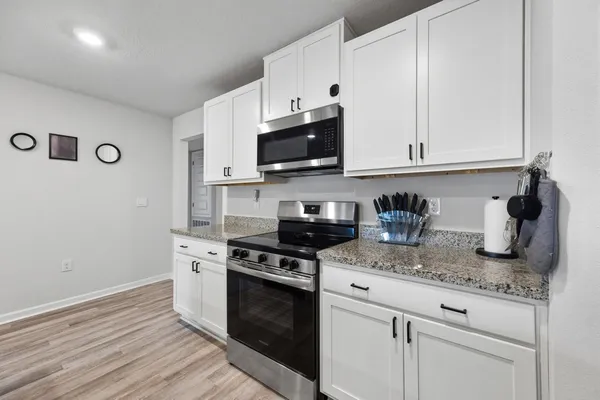 a kitchen with granite countertop white cabinets appliances and wooden floor