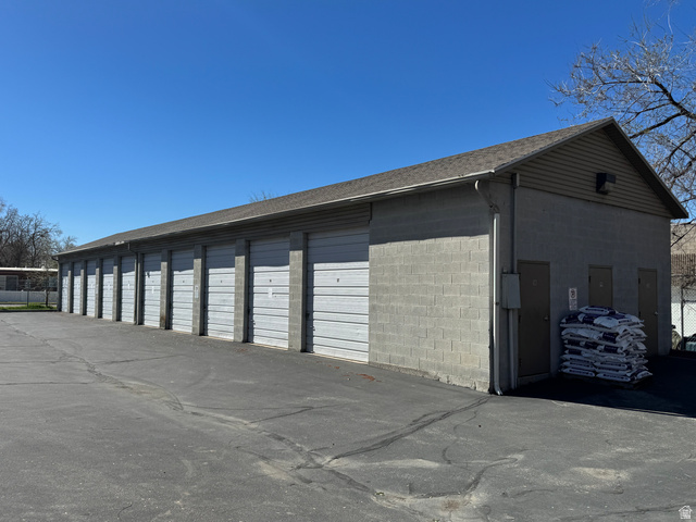 1115 North Main Street Bountiful, UT 84010 - Photo 9 of 17 Self-storage facility featuring multiple roll-up garage doors, concrete block construction, a sloped shingle roof, and a paved asphalt drive