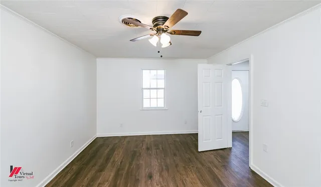 a view of an empty room with wooden floor and a ceiling fan