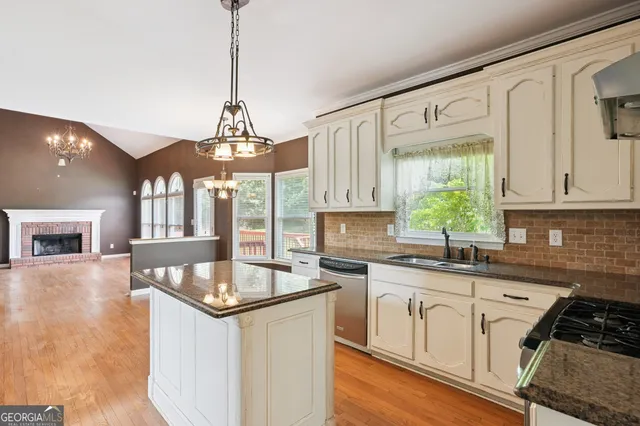 a kitchen with stainless steel appliances granite countertop a stove a sink dishwasher and white cabinets with wooden floor