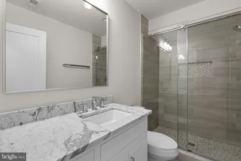 a bathroom with a granite countertop sink a toilet a mirror and shower