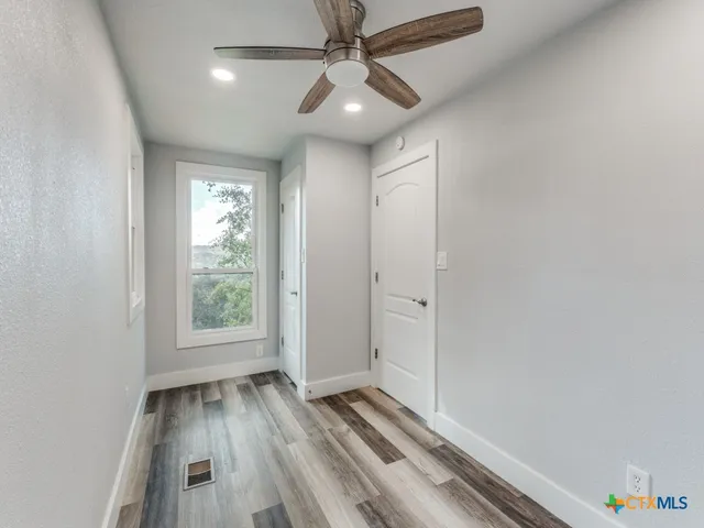 an empty room with wooden floor chandelier fan and windows