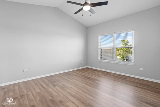 an empty room with wooden floor chandelier fan and windows