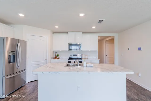 a kitchen with stainless steel appliances a sink stove refrigerator and white cabinets with wooden floor