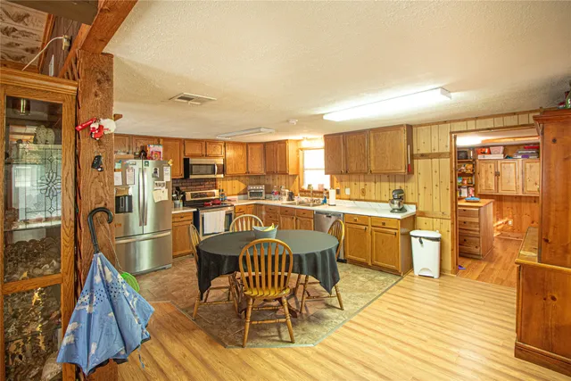a kitchen with stainless steel appliances a stove a sink dishwasher a refrigerator with a dining table and chairs