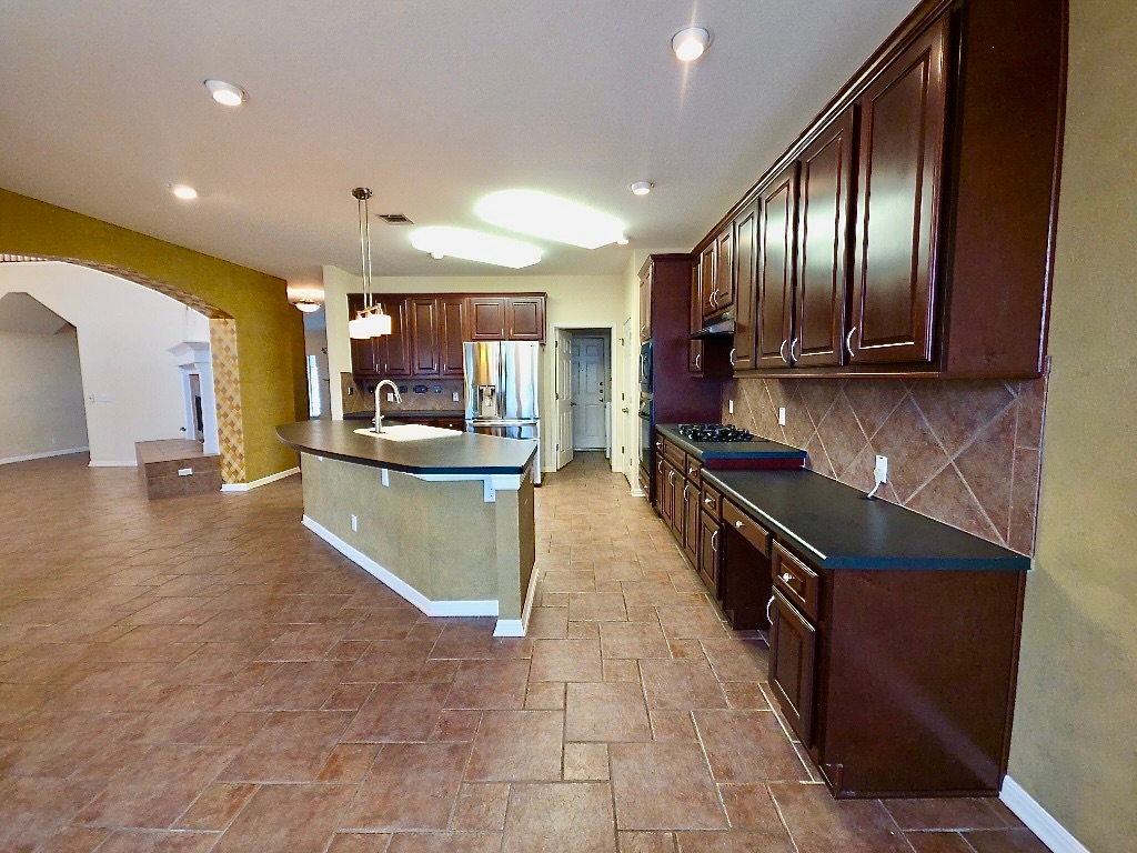 1103 Seton Hall Lane Pflugerville, TX 78660 - Photo 10 of 32 Kitchen with dark countertops, arched walkways, dark brown cabinets, hanging light fixtures, and stone finish floors