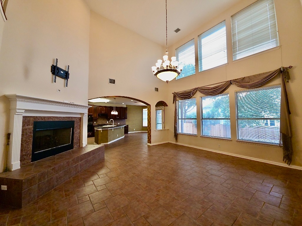 1103 Seton Hall Lane Pflugerville, TX 78660 - Photo 4 of 32 Unfurnished living room with a fireplace, arched walkways, healthy amount of natural light, a high ceiling, stone tile floors and a view to the backyard.