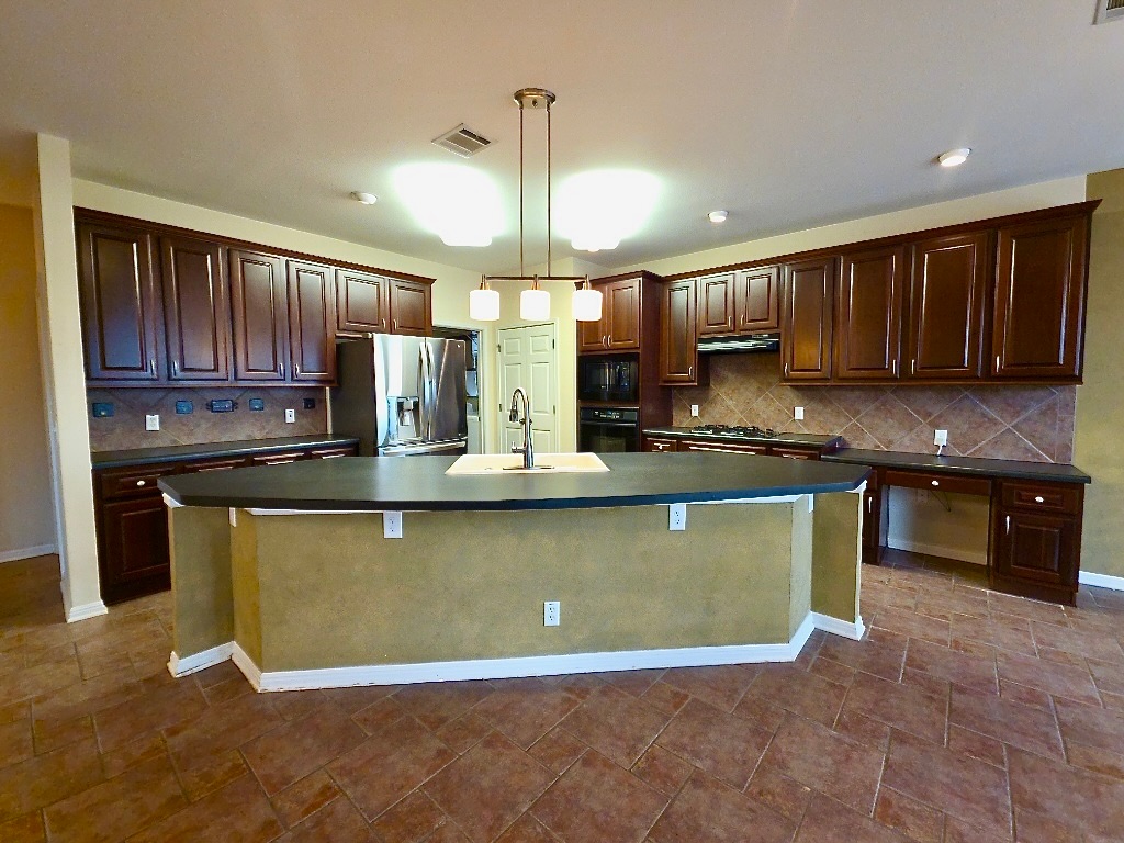 1103 Seton Hall Lane Pflugerville, TX 78660 - Photo 7 of 32 Kitchen with dark brown cabinets, large center island; backsplash, and dark countertops
