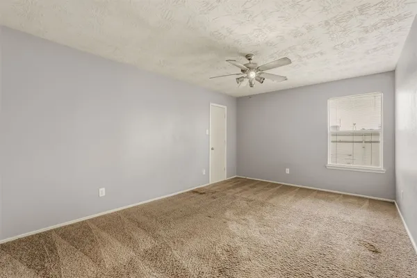 an empty room with chandelier fan and windows