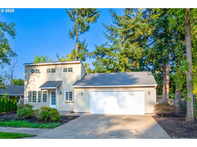 a view of a white house with a yard plants and large tree