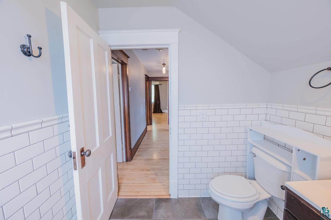508 10th Street South Virginia, MN 55792 - Photo 27 of 43 Bathroom featuring white subway tile wainscoting, a toilet with an over-the-toilet storage unit, and dark grey floor tiles