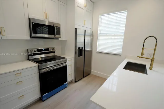 a kitchen with a sink dishwasher and white cabinets with wooden floor