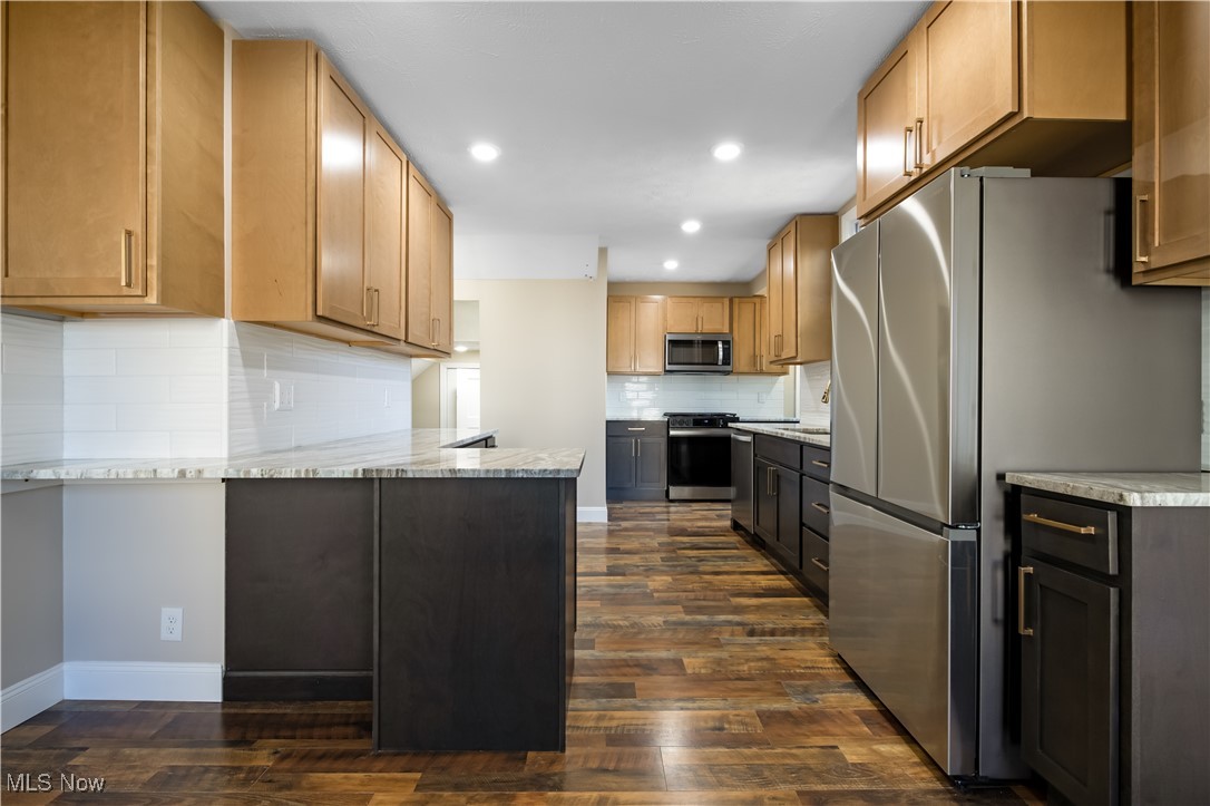 3716 Rolliston Road Cleveland, OH 44120 - Photo 13 of 37 Kitchen with stainless steel appliances, light stone counters, decorative backsplash, dark wood-style floors, and a peninsula