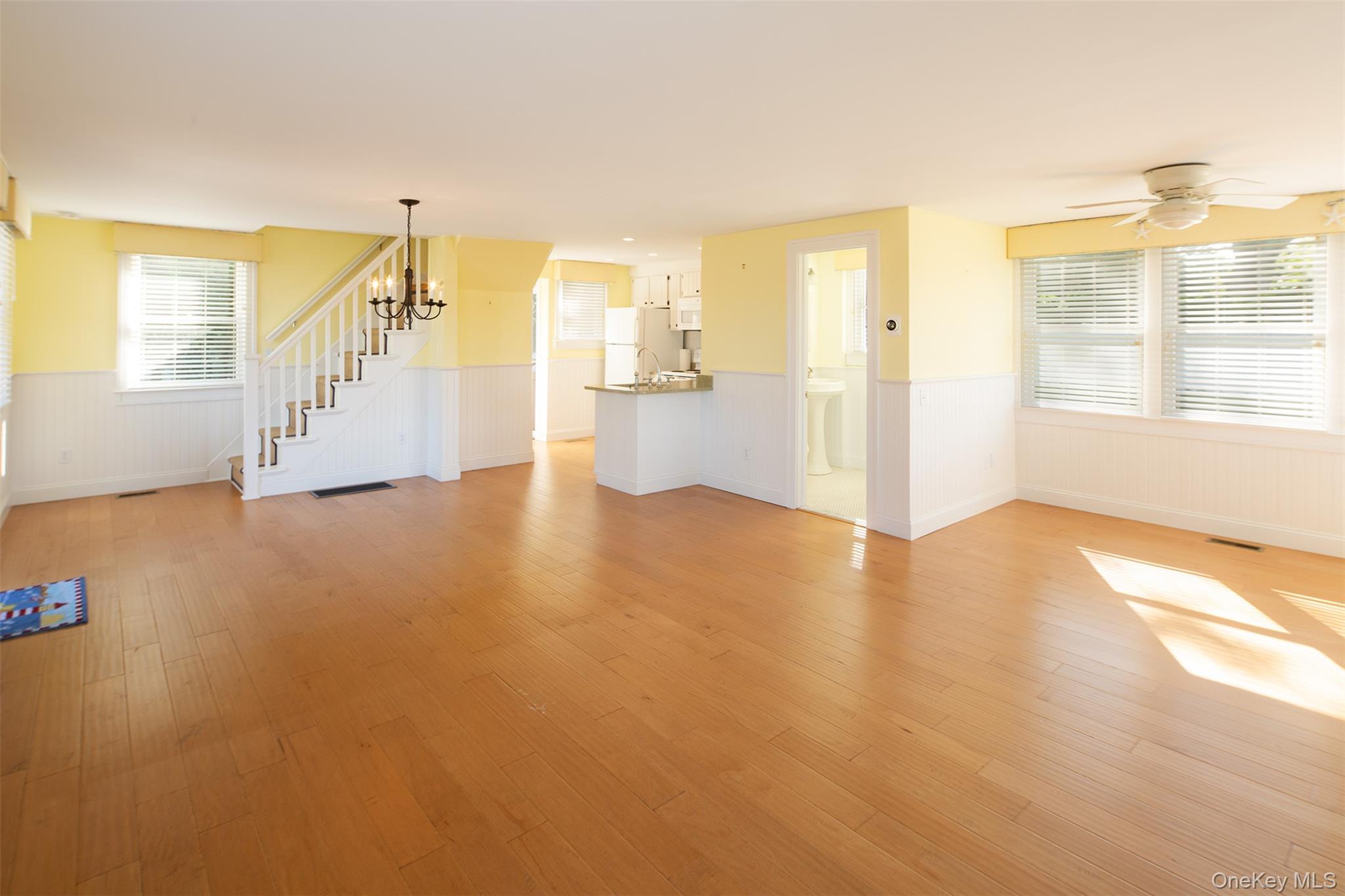 1 Canal Road Hampton Bays, NY 11946 - Photo 15 of 50 Unfurnished living room featuring healthy amount of natural light, light wood-style flooring, wainscoting, stairway, and a ceiling fan