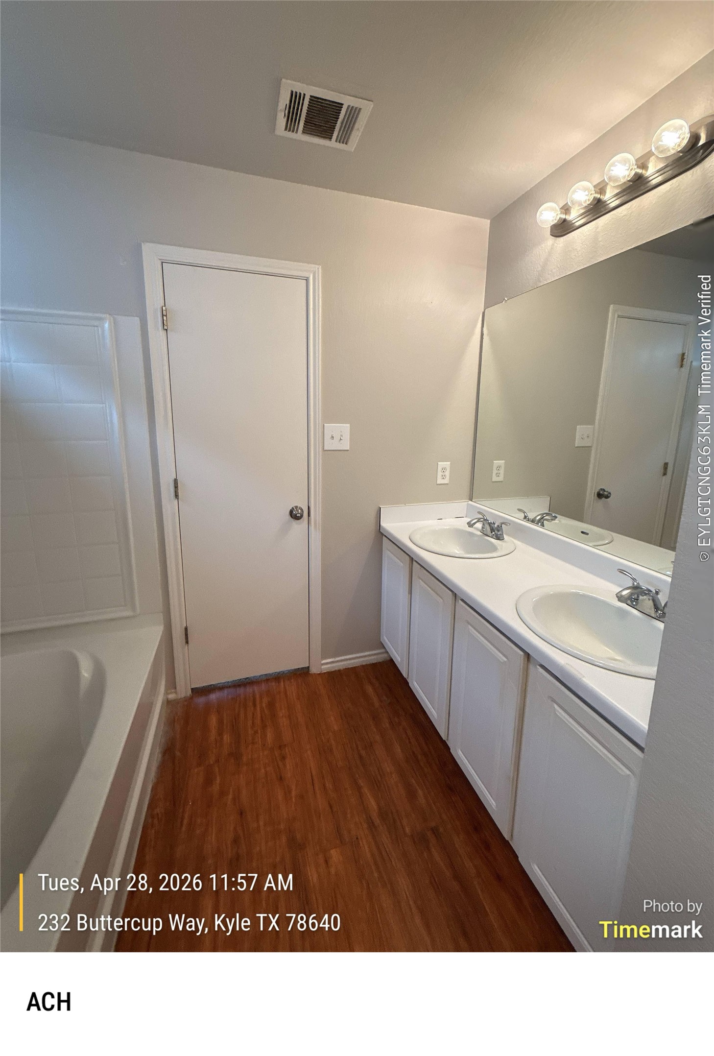 232 Buttercup Way Kyle, TX 78640 - Photo 13 of 17 Bathroom featuring a dual vanity with white cabinetry, wood-finish flooring, a full-width mirror, and a white bathtub with tile surround