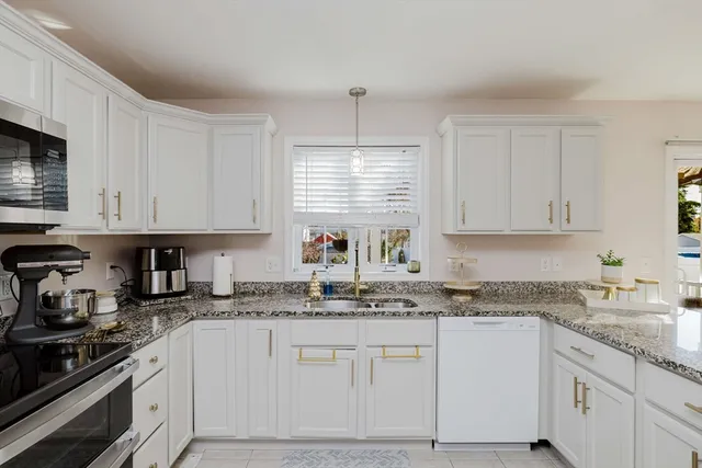 a kitchen with granite countertop white cabinets white stainless steel appliances a sink and a window