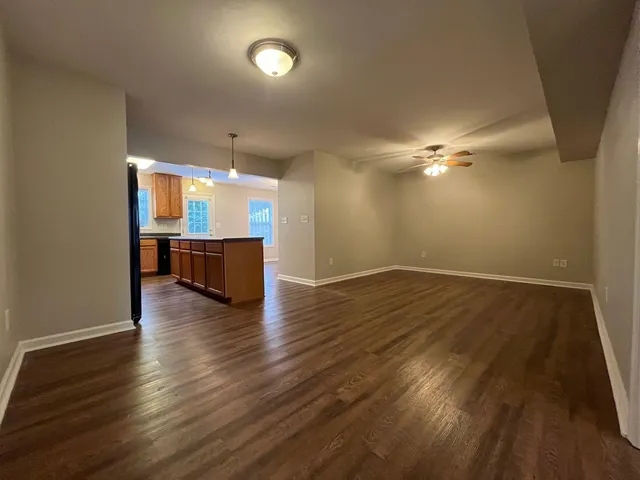 an empty room with wooden floor and way to kitchen