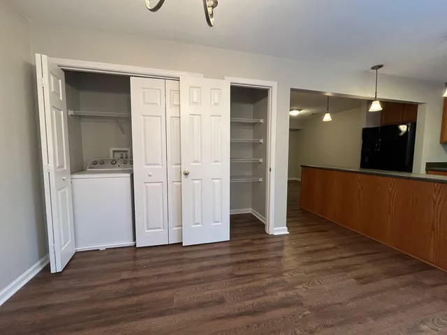 an empty room with wooden floor and way to kitchen