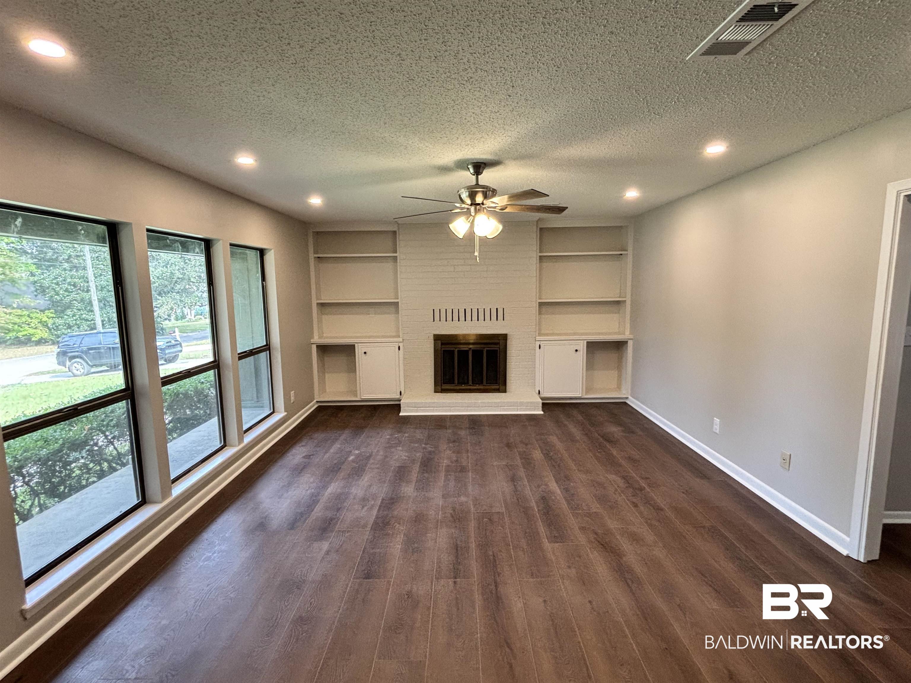 10 Soldiers Route Daphne, AL 36527 - Photo 5 of 26 Unfurnished living room with a textured ceiling, dark wood-style flooring, a brick fireplace, recessed lighting, and built in features