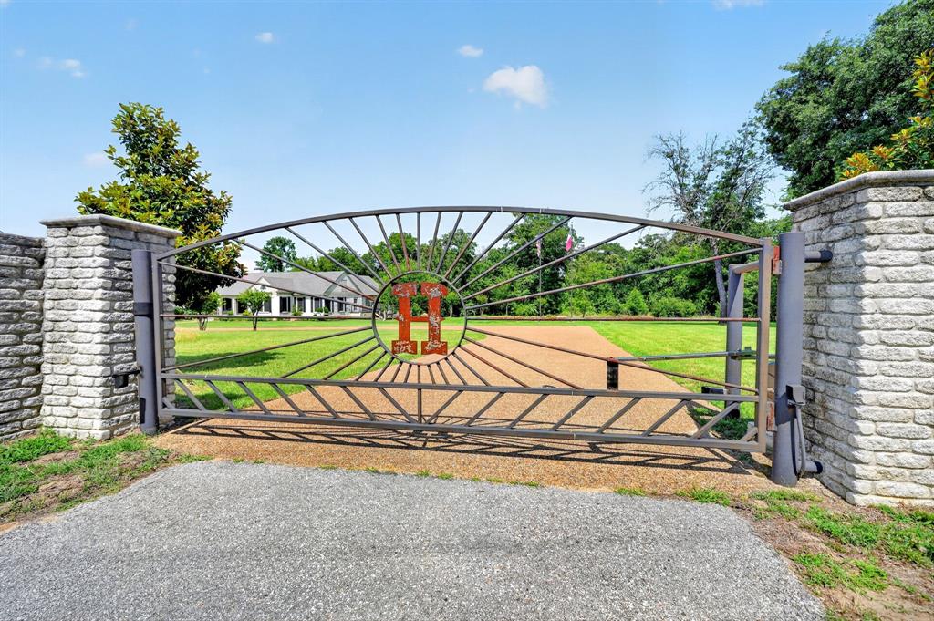 1901 Rose Pointe Athens, TX 75752 - Photo 3 of 37 Automated metal gate with stone-clad pillars, gravel driveway, and expansive manicured lawn