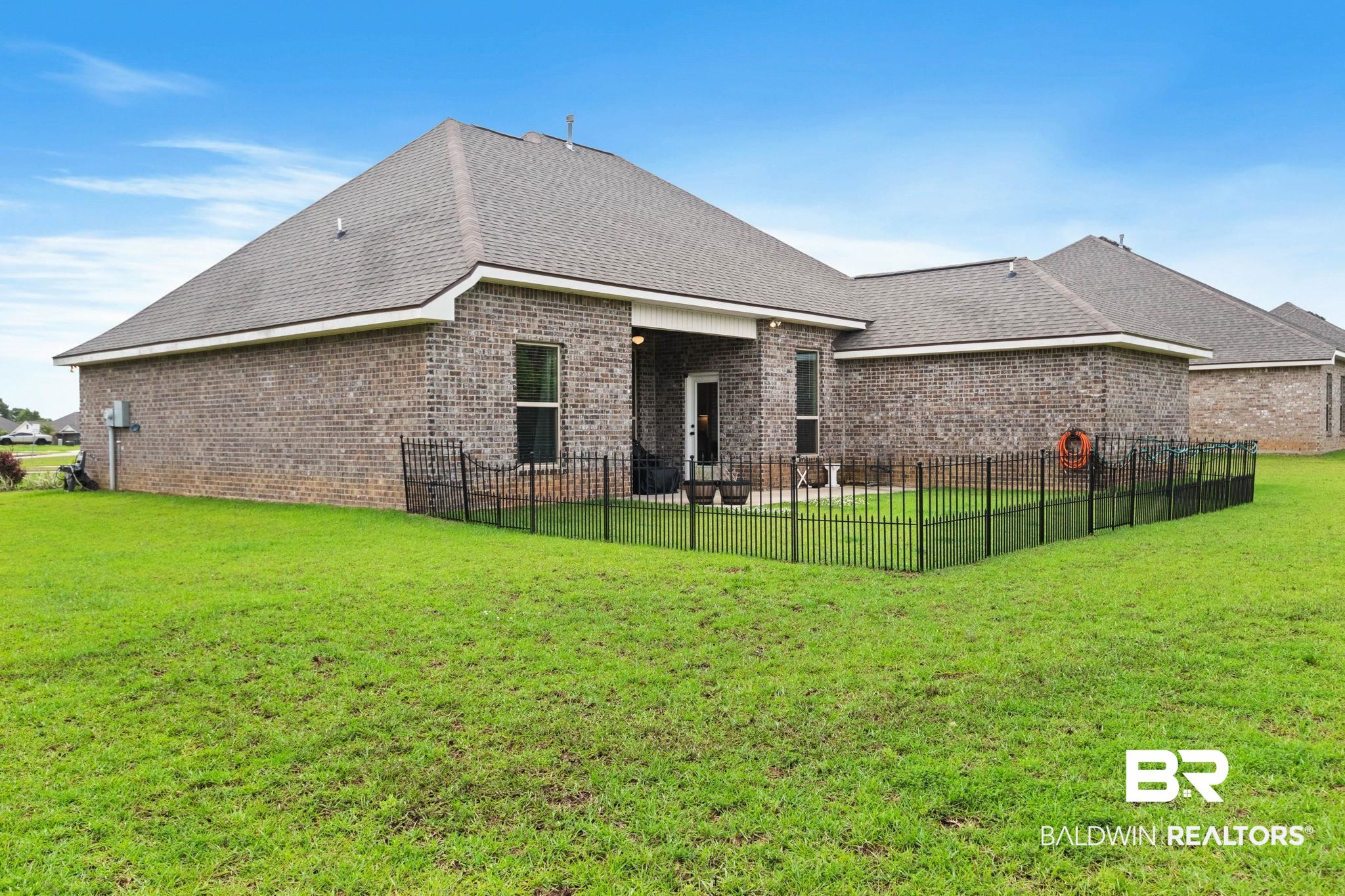 22244 Hibiscus Circle Foley, AL 36535 - Photo 7 of 51 Expansive green lawn surrounds a brick exterior home with a partial black metal fence enclosing a patio area