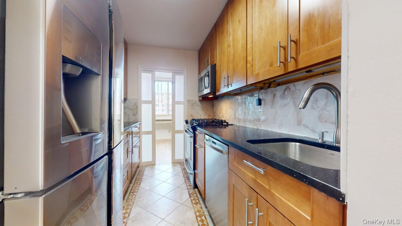 118-17 Union Turnpike, Unit 18H Queens, NY 11375 - Photo 14 of 49 Kitchen featuring stainless steel appliances, light tile patterned flooring, brown cabinetry, dark stone countertops, and decorative backsplash