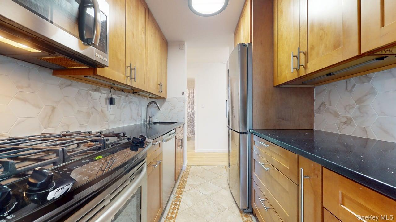 118-17 Union Turnpike, Unit 18H Queens, NY 11375 - Photo 15 of 49 Kitchen featuring stainless steel appliances, dark stone counters, tasteful backsplash, light tile patterned floors, and brown cabinets