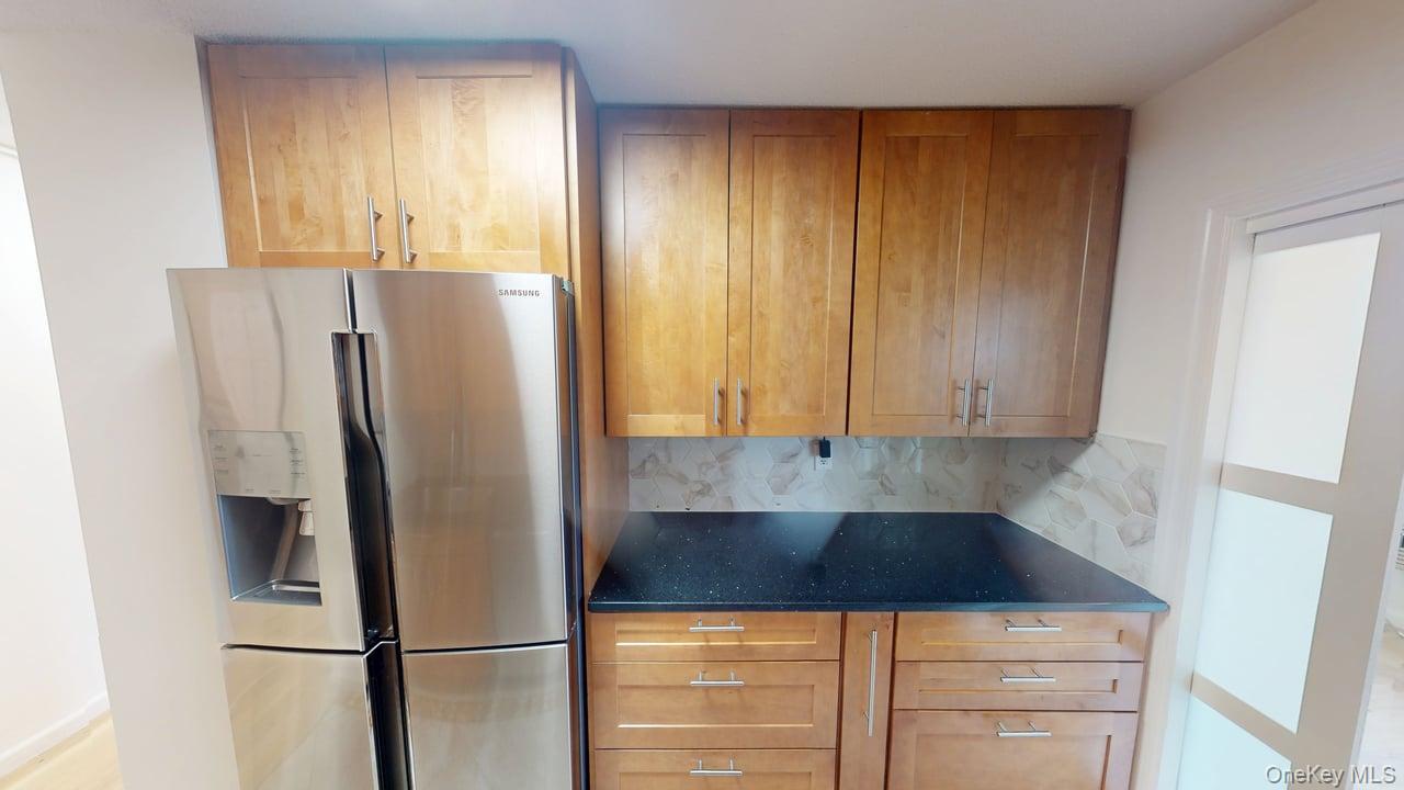 118-17 Union Turnpike, Unit 18H Queens, NY 11375 - Photo 17 of 49 Kitchen with stainless steel refrigerator with ice dispenser, dark stone countertops, tasteful backsplash, and brown cabinets