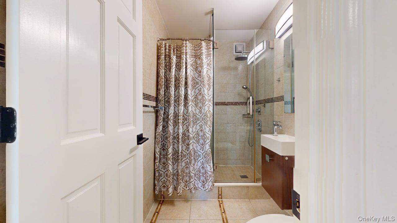 118-17 Union Turnpike, Unit 18H Queens, NY 11375 - Photo 32 of 49 Full bathroom with vanity, a stall shower, light tile patterned floors, and tile walls