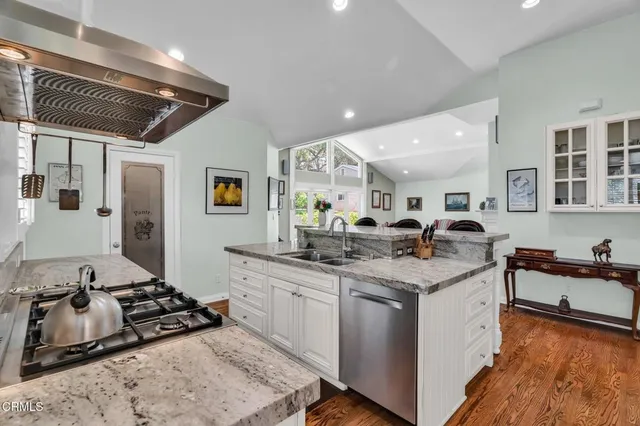 a kitchen with stainless steel appliances granite countertop a stove top oven a sink a dining table and chairs with wooden floor