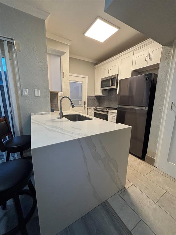 11655 Audelia Road, Unit 1304 Dallas, TX 75243 - Photo 2 of 11 Kitchen featuring a textured wall, light stone counters, white cabinets, ornamental molding, and stainless steel appliances