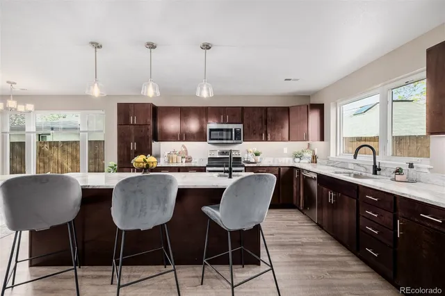 a kitchen with stainless steel appliances granite countertop a sink a stove a refrigerator cabinets and a dining table with wooden floor