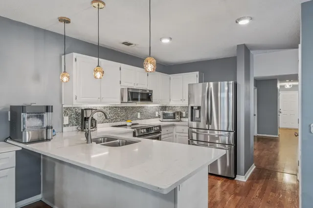 a kitchen with stainless steel appliances a stove a sink a refrigerator a center island a stove and white cabinets with wooden floor