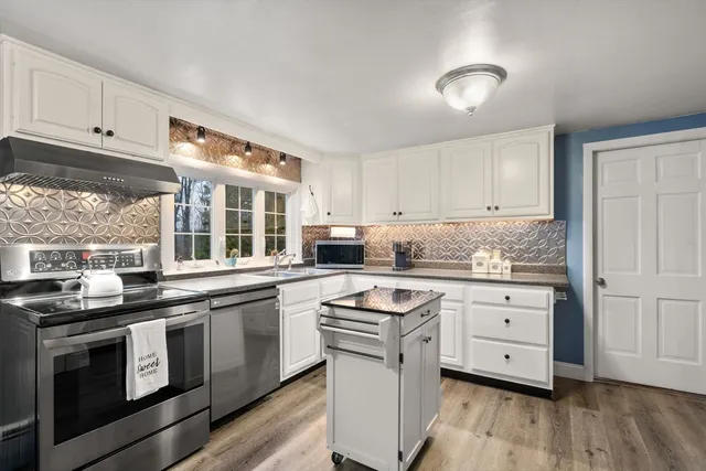 a kitchen with stainless steel appliances granite countertop a stove a sink and white cabinets