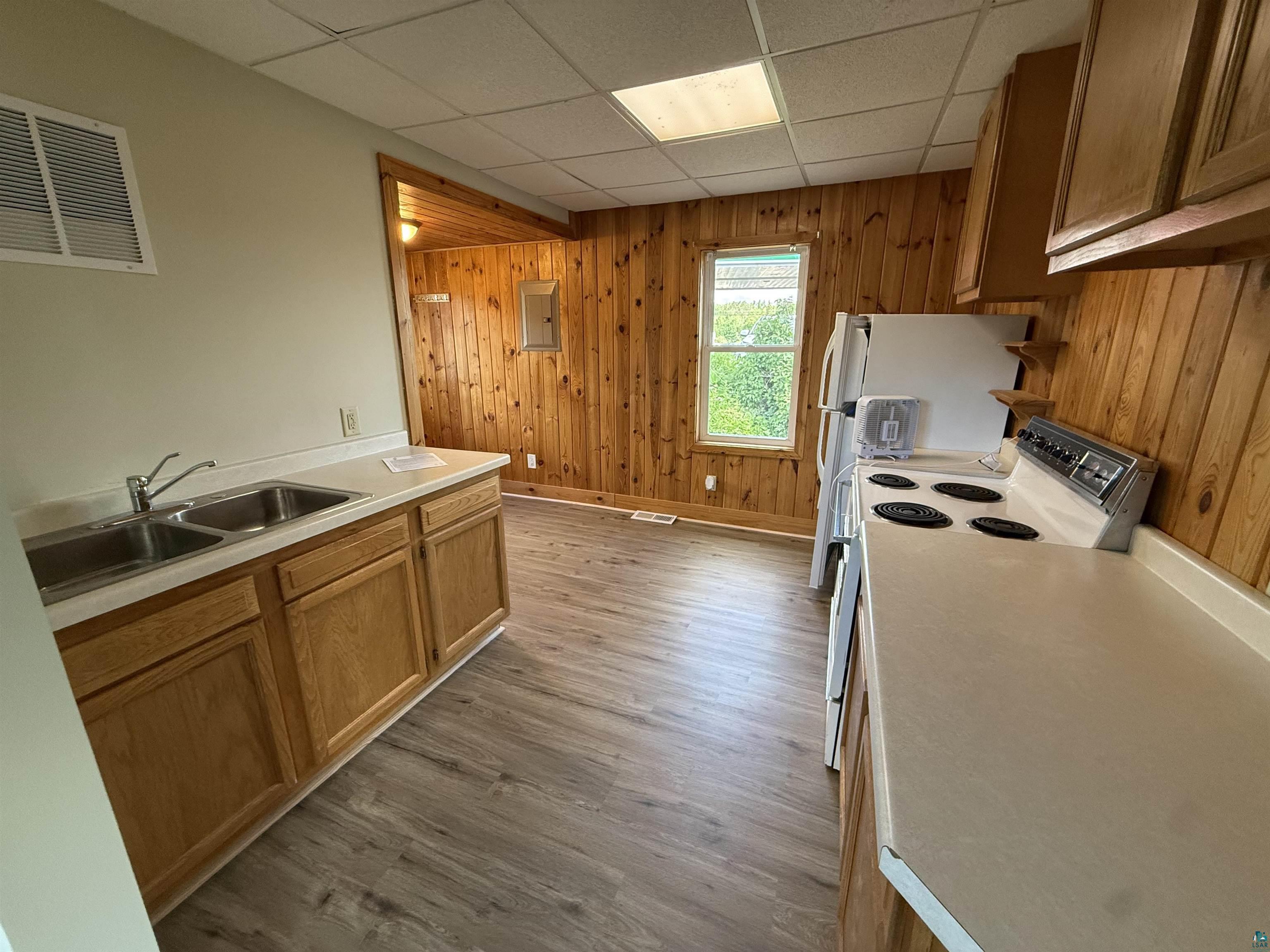 3841 Haines Road Hermantown, MN 55811 - Photo 3 of 11 Kitchen featuring wood-finish flooring, natural wood paneling, wood cabinetry, dual basin stainless steel sink, and a drop ceiling with recessed lighting