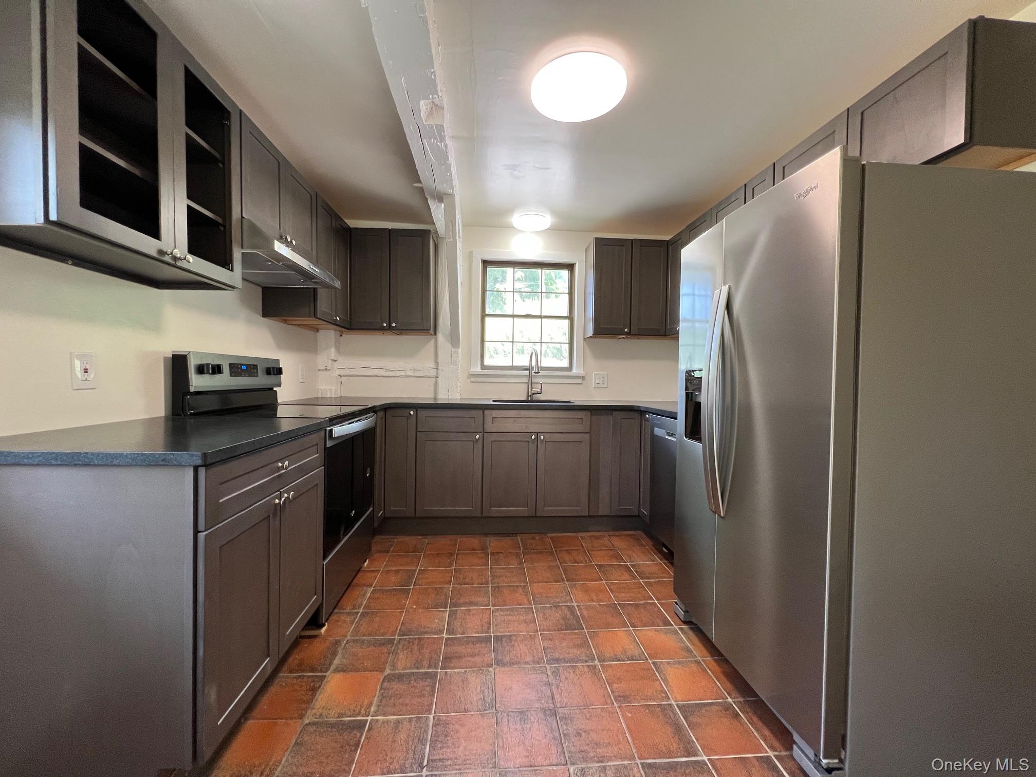 Kitchen featuring stainless steel appliances, dark countertops, under cabinet range hood, stone finish flooring, and open shelves