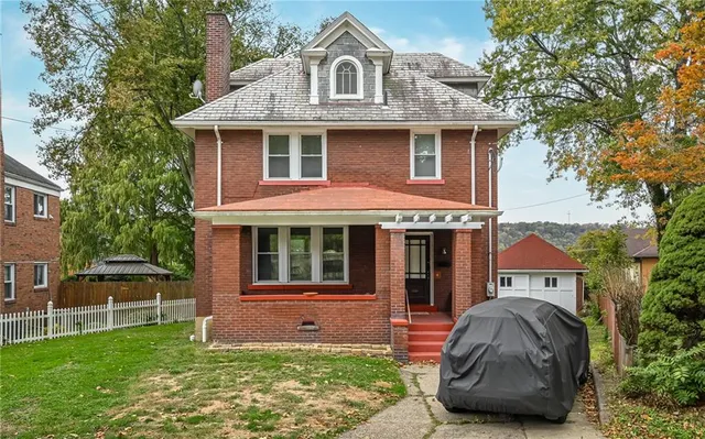 a view of a brick house with a yard plants and a large tree