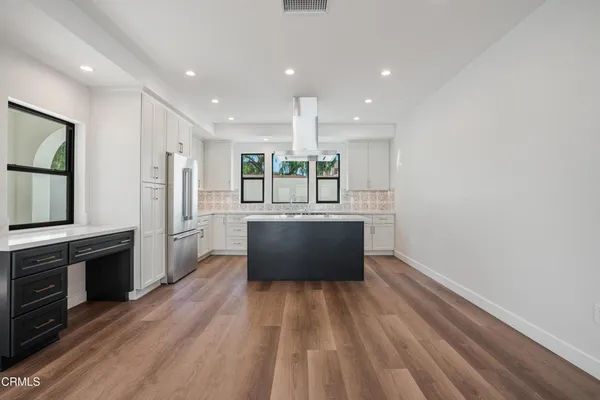 a large kitchen with a center island wooden floor and stainless steel appliances