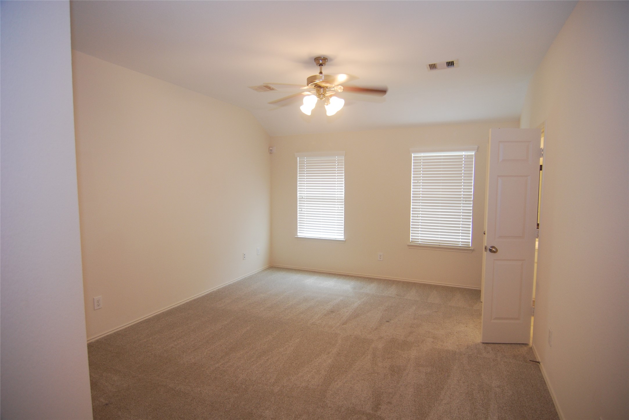 2834 Lockeridge Pines Drive Spring, TX 77386 - Photo 10 of 20 This is a bright, carpeted bedroom with neutral walls, featuring a ceiling fan and two windows with blinds. A door opens to an adjacent room or hallway.