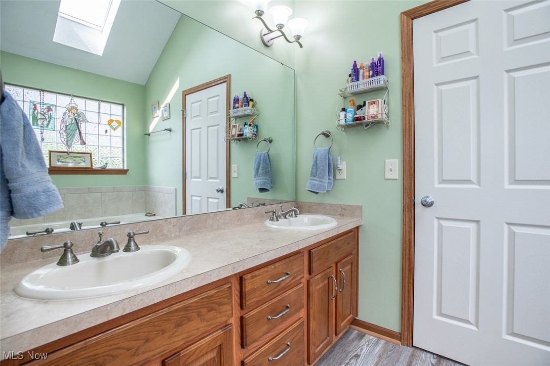 126 Timber Ridge Drive Elyria, OH 44035 - Photo 31 of 49 Bathroom featuring a skylight, double vanity, a bath, lofted ceiling, and wood finished floors