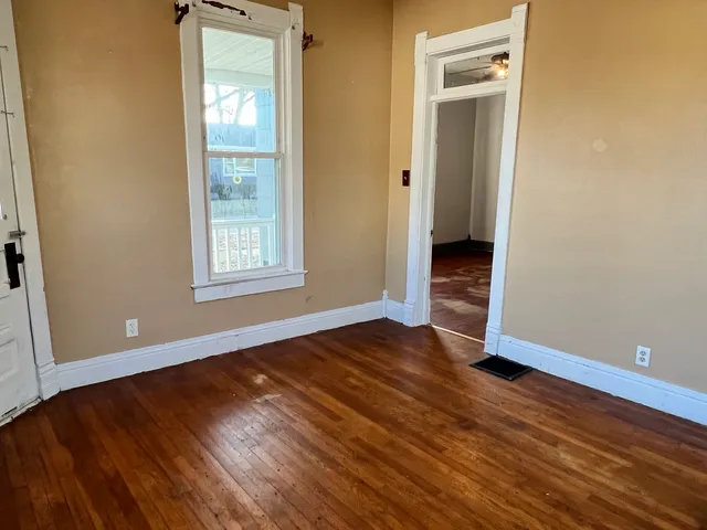 a view of an empty room with wooden floor and a window