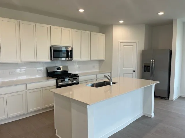 a kitchen with stainless steel appliances a sink a stove a refrigerator a center island and cabinets