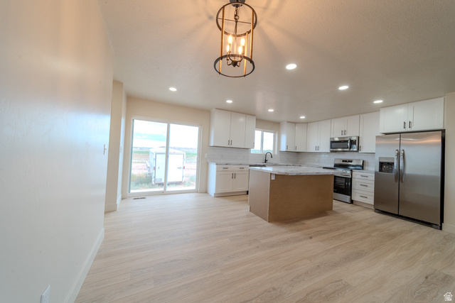 130 Pole Line Road, Unit 2 Roosevelt, UT 84066 - Photo 8 of 33 Open-concept kitchen featuring light wood-finish flooring, white cabinetry, a central island with a contrasting base, stainless steel appliances, and a sliding glass door