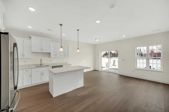 a kitchen with stainless steel appliances granite countertop a stove a sink a refrigerator white cabinets and wooden floor next to a window