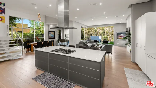 a living room with stainless steel appliances furniture a rug kitchen view and a large window