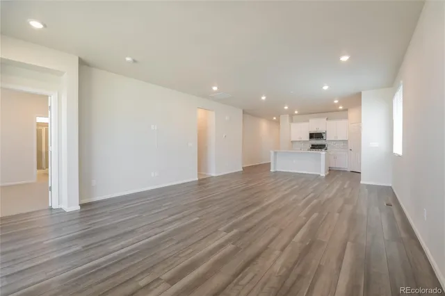 a view of an empty room with wooden floor and a kitchen
