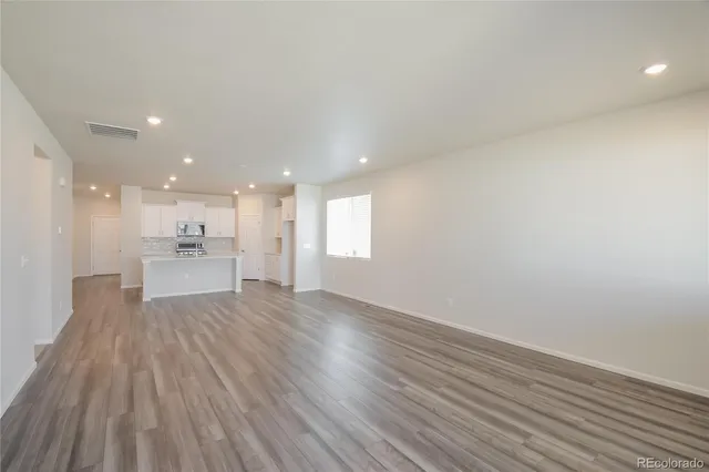 a view of an empty room with wooden floor and a kitchen