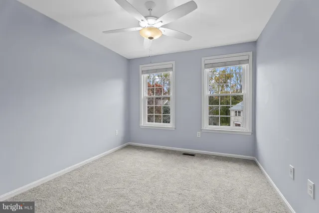 an empty room with chandelier fan and windows