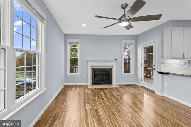 a view of a livingroom with a fireplace a ceiling fan and wooden floor